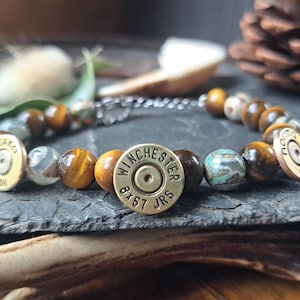 May include: A brown and gold bracelet with tiger's eye beads, agate beads, and two brass bullet casings. The bullet casings are engraved with "Sako 40.06" and "Winchester 8x57 JRS".