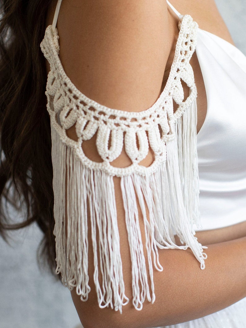 May include: White crochet shoulder piece with fringe detail. The crochet is made with a delicate pattern and the fringe is long and flowing.