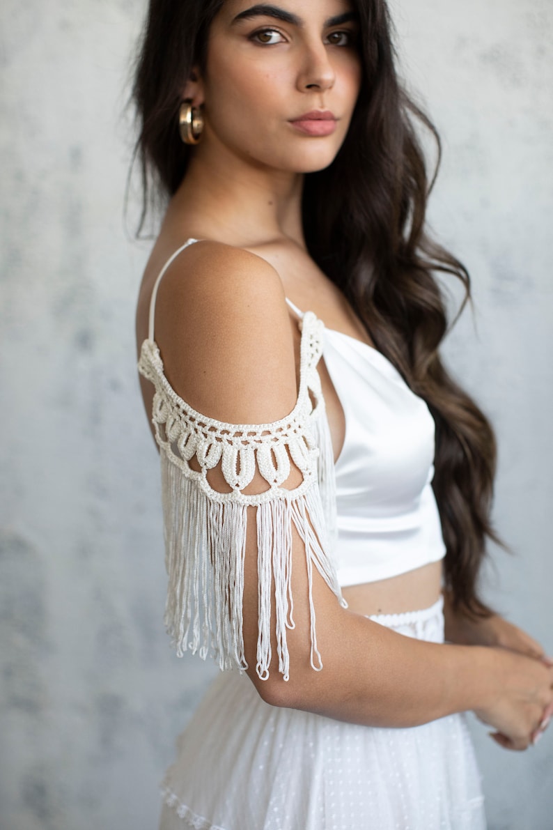 May include: A white satin crop top with a crocheted off-the-shoulder detail and fringe trim.