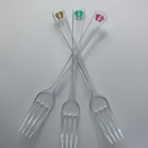 Peut inclure: Trois fourchettes en plastique transparent avec des empreintes de pieds dor&eacute;es, vertes et roses imprim&eacute;es sur les manches.