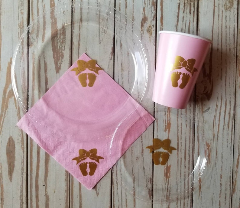 Peut inclure: Articles de f&ecirc;te de baby shower roses et dor&eacute;s. Un gobelet en papier rose avec un motif d'empreinte de pied de b&eacute;b&eacute; dor&eacute;, une serviette en papier rose avec un motif d'empreinte de pied de b&eacute;b&eacute; dor&eacute; et une assiette en plastique transparente avec un motif d'empreinte de pied de b&eacute;b&eacute; dor&eacute;.
