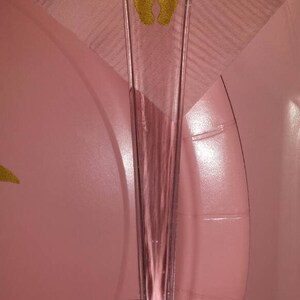 Peut inclure: Un serveur &agrave; g&acirc;teau en plastique transparent avec un motif de petite empreinte de pied dor&eacute;e. Le serveur est sur une surface rose.