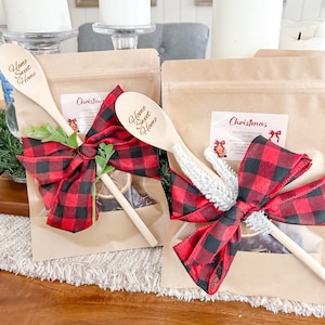 May include: Two kraft paper bags with Christmas labels, tied with red and black buffalo plaid bows. Wooden spoons with "Home Sweet Home" are included. The bags contain potpourri and are decorated with greenery and dried citrus.