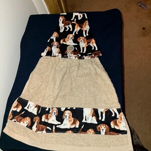 May include: A beige kitchen towel with a black border and top section, both patterned with brown and white beagle dogs. The towel is hanging on a dark blue surface.