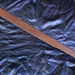 Puede incluir: Una paleta de madera marrón con forma rectangular y un mango redondeado con un agujero. La paleta está sobre una tela azul oscuro brillante.