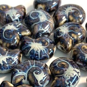 May include: A collection of ceramic beads in a dark blue and white swirl pattern. The beads are shaped like seashells and have a glossy finish.