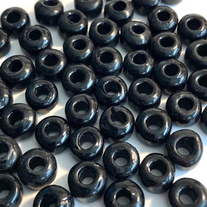 May include: A large quantity of black plastic beads with a hole in the center. The beads are round and have a glossy finish.