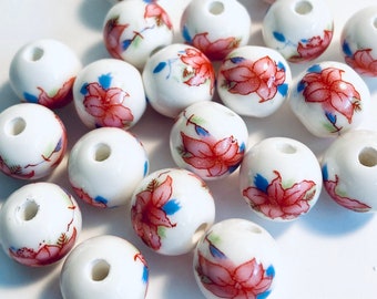 May include: White ceramic beads with a floral design. Each bead features a red and pink flower with blue and green accents. The beads are round with a hole through the center, suitable for jewelry making or crafts.