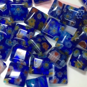 May include: A collection of small, square, blue glass tiles with a white background and colorful floral patterns. The tiles are translucent and have a glossy finish.