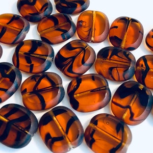 May include: A collection of brown and black glass beads with a swirl pattern. The beads are oval shaped and have a glossy finish.