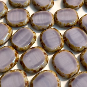 May include: A collection of oval-shaped, light purple glass beads with brown speckles. The beads have a smooth, glossy finish.