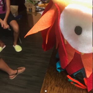 Puede incluir: Un juguete de b&uacute;ho de fieltro colorido con un ojo blanco grande y una pupila negra. El b&uacute;ho est&aacute; hecho de fieltro rojo, naranja, amarillo y azul.