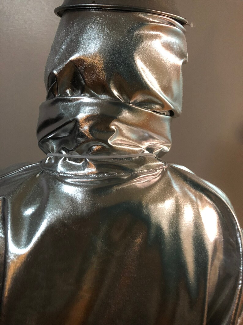 K&ouml;nnte beinhalten: Ein silberner, metallischer Overall mit Kapuze und gl&auml;nzender, reflektierender Oberfl&auml;che.