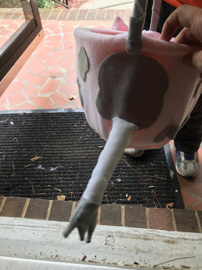 Puede incluir: Un cubo de truco o trato de vaca rosa y gris con un brazo largo, blanco y peludo y una mano gris.