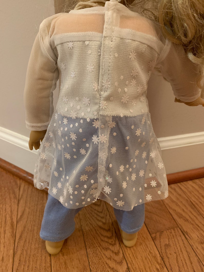 May include: A doll wearing a white mesh top with a floral pattern over a white top and light blue jeans. The mesh top has long sleeves and a flared hem. The doll's blonde hair is visible.