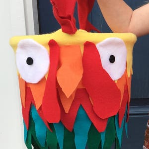 Puede incluir: Una bolsa de truco o trato de fieltro rojo, naranja, amarillo, verde y azul en forma de gallo con ojos blancos y una pupila negra.