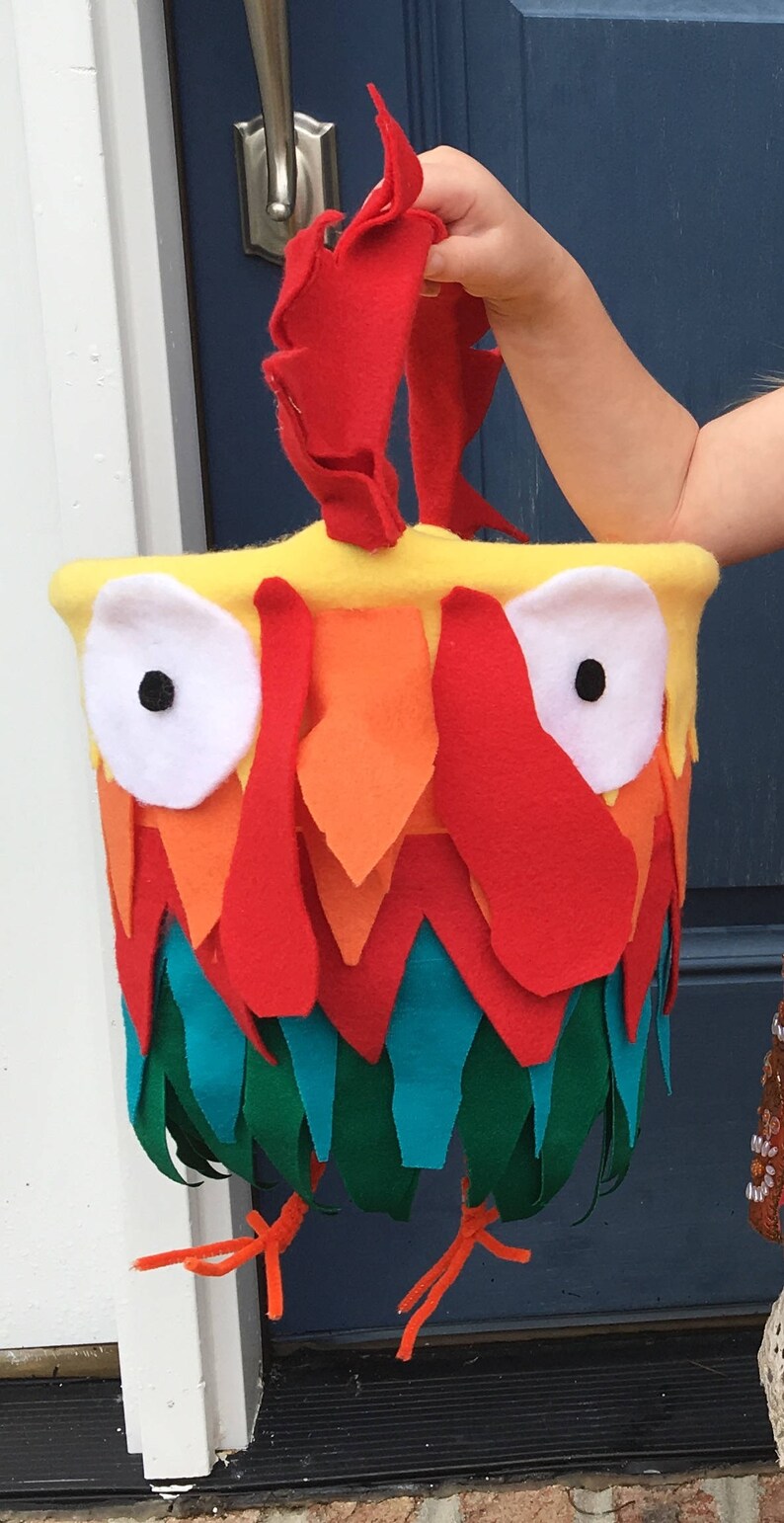 Puede incluir: Una bolsa de truco o trato de fieltro rojo, naranja, amarillo, verde y azul en forma de gallo con ojos blancos y una pupila negra.