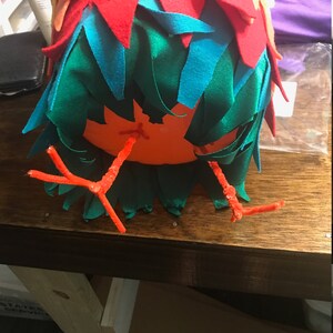 Puede incluir: Una artesan&iacute;a de fieltro rojo, naranja y verde con patas de limpiapipas naranja. La artesan&iacute;a tiene forma de p&aacute;jaro.