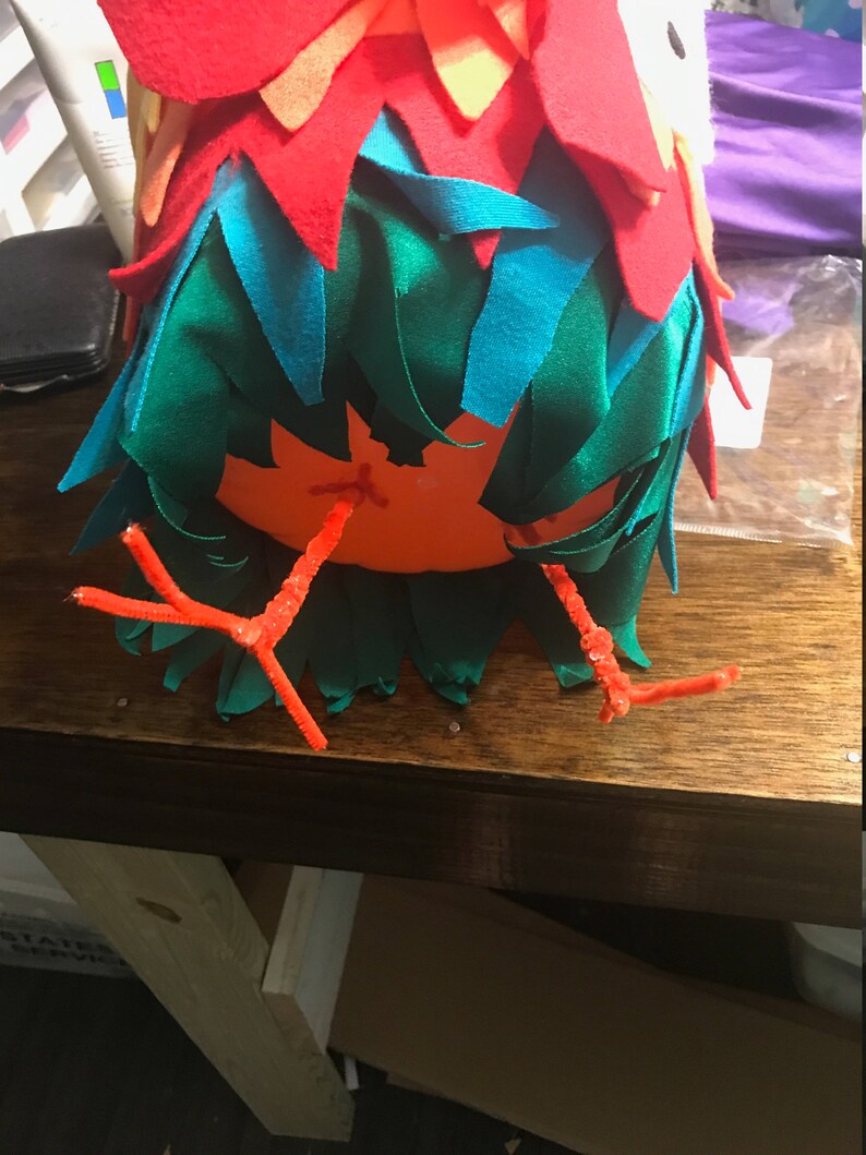 Puede incluir: Una artesan&iacute;a de fieltro rojo, naranja y verde con patas de limpiapipas naranja. La artesan&iacute;a tiene forma de p&aacute;jaro.
