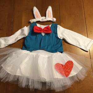May include: White tutu with a red heart, a blue vest with a red bow tie, and white bunny ears headband.
