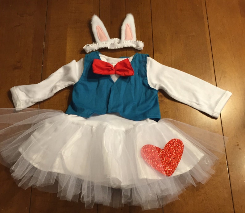 May include: White tutu with a red heart, a blue vest with a red bow tie, and white bunny ears headband.