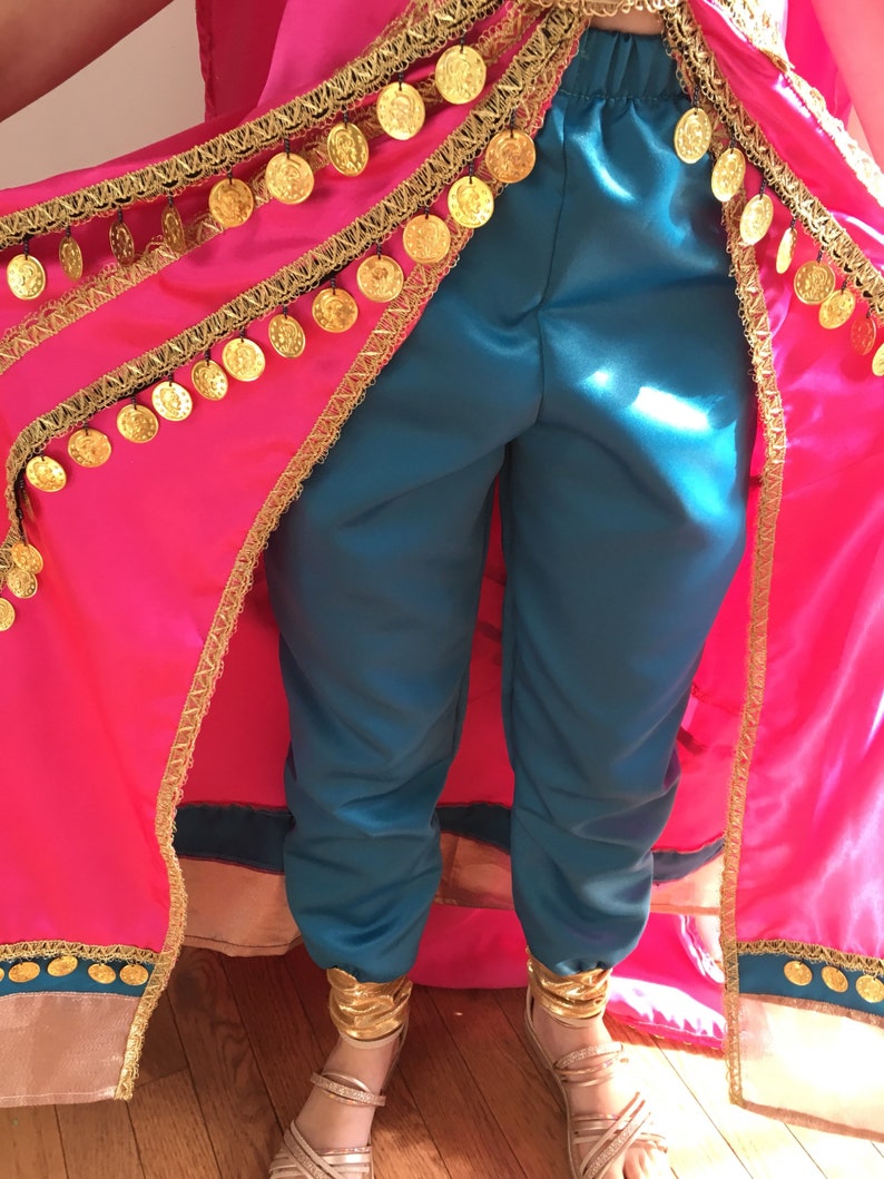 May include: A turquoise pair of pants with gold coin trim and a pink cape with gold trim. The cape is open in the front, revealing the pants.