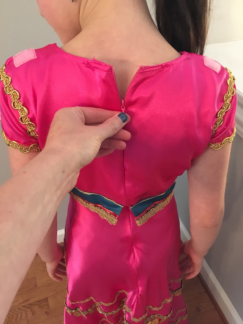 May include: A pink dress with gold trim and a zipper in the back. The dress has a blue and gold sash around the waist.