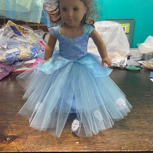 May include: A blue and white tulle dress with a floral pattern and a sweetheart neckline. The dress has a layered skirt and is decorated with white flowers.
