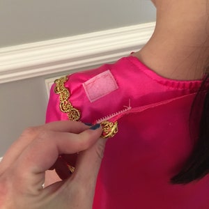May include: A pink satin dress with gold trim and a white fabric patch on the shoulder.