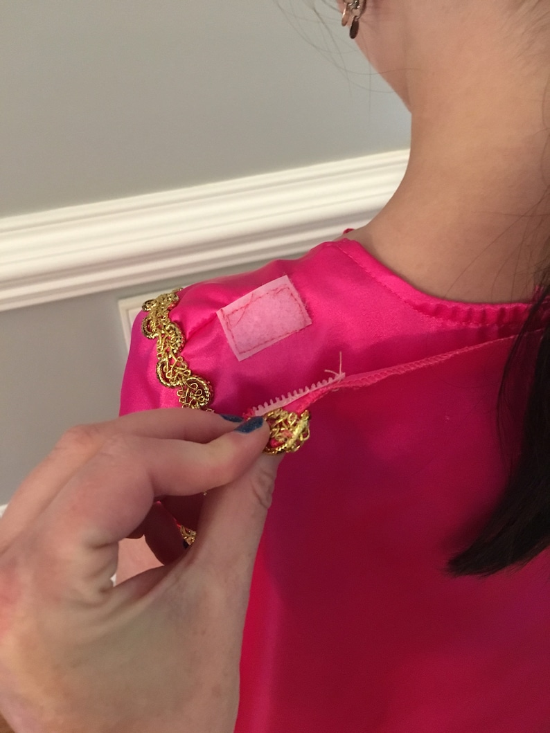 May include: A pink satin dress with gold trim and a white fabric patch on the shoulder.