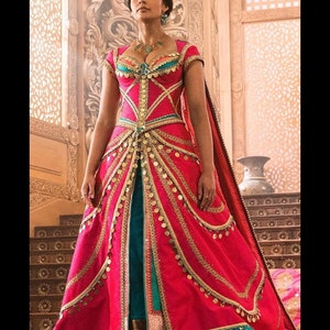 May include: A woman in a pink and teal gown with gold accents and a long train. She is standing on a wooden platform with intricate carvings.