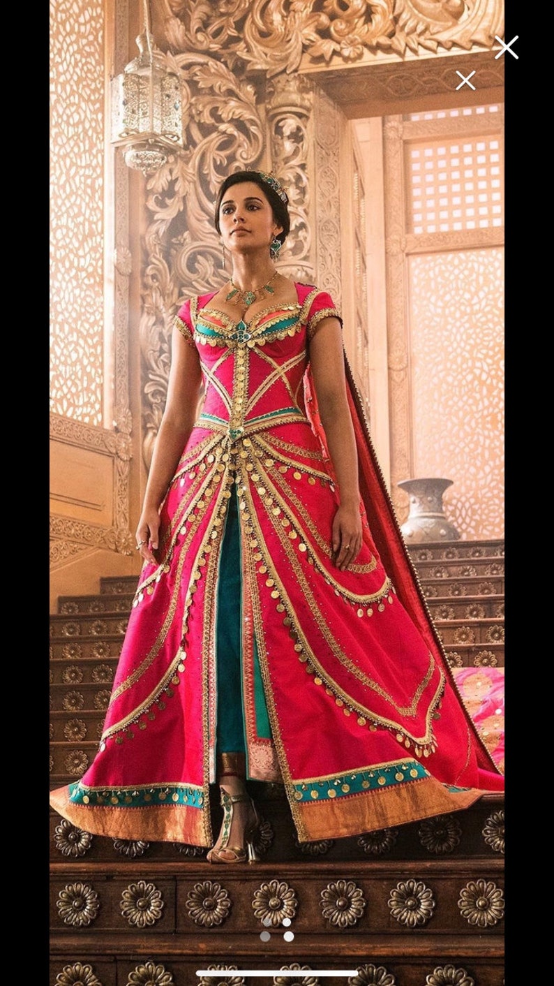 May include: A woman in a pink and teal gown with gold accents and a long train. She is standing on a wooden platform with intricate carvings.