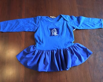 May include: A blue baby dress with a ruffled skirt and a blue embroidered Duke University logo on the front.