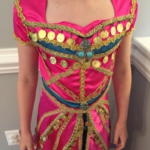 May include: A pink dress with gold and blue trim. The dress has a sweetheart neckline and is decorated with gold coins.