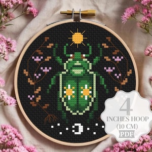 May include: A cross-stitch pattern in a 10 cm wooden hoop featuring a green beetle on a black background. The beetle has white and yellow floral markings, a yellow sun above, and branches with pink flowers on each side. A white crescent moon is below.
