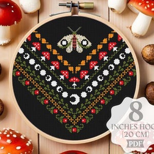 May include: A cross-stitch embroidery hoop with a black background featuring a moth and mushroom design. The hoop is 8 inches (20 cm) in diameter. The image also includes several red and white spotted mushrooms and brown nuts.
