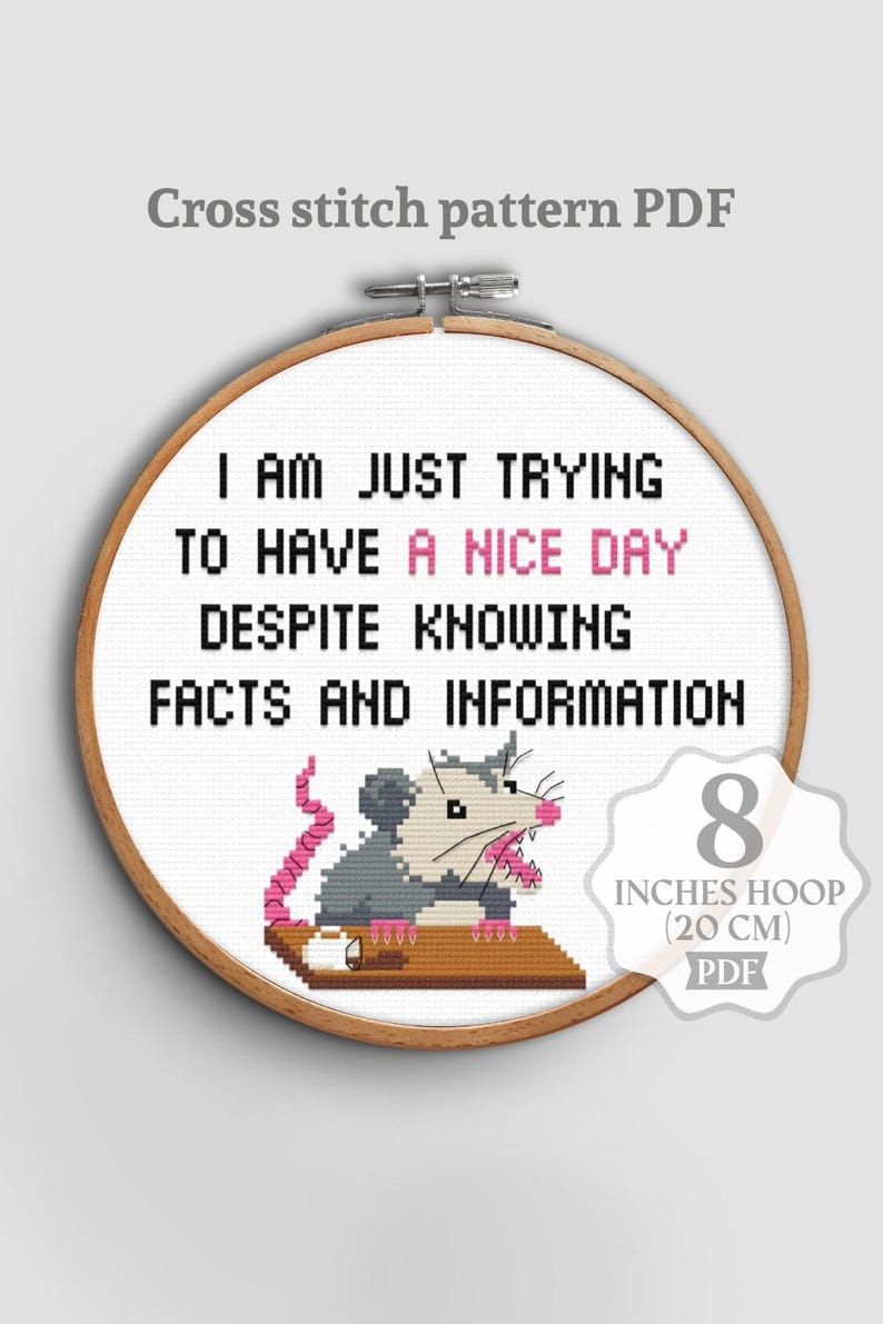 Op de afbeelding: PDF kruissteekpatroon met een humoristische quote: "I AM JUST TRYING TO HAVE A NICE DAY DESPITE KNOWING FACTS AND INFORMATION." Het ontwerp bevat een grijze opossum met roze accenten. De borduurring is 20 cm.