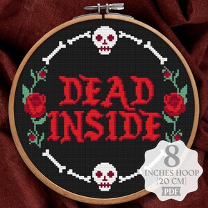 May include: A cross-stitch pattern in an 8 inches hoop featuring the text DEAD INSIDE in red block letters. The design includes two white skulls, white bones arranged in a circle, and red roses with green stems on a black fabric background.