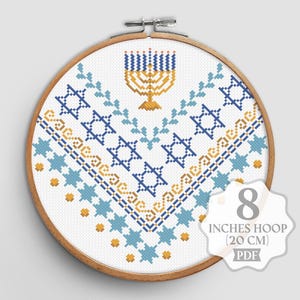 May include: A cross-stitch embroidery hoop featuring a menorah and Star of David design in blue and gold. The design is on white fabric and set in a 20 cm hoop. The PDF pattern is available.