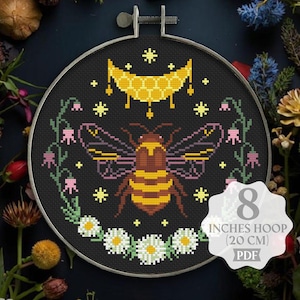 May include: Cross stitch pattern featuring a bee with a honeycomb moon and floral accents on a black background. The pattern is designed for an 8-inch hoop (20 cm) and is available as a PDF download.
