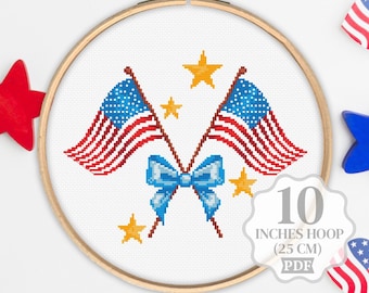 May include: A cross-stitch design featuring two American flags, a blue bow, and gold stars, set within a 10-inch (25 cm) embroidery hoop. The design is in red, white, and blue, with a PDF option.