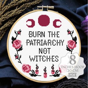 May include: A circular wooden embroidery hoop containing white fabric with a cross-stitch design. The text reads BURN THE PATRIARCHY NOT WITCHES, surrounded by pink roses, black leaves, moon phases, and candles. The hoop measures 8 inches in diameter.