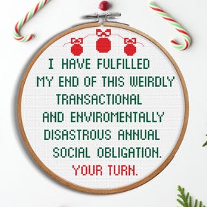 Op de afbeelding: Een borduurring met de tekst "I HAVE FULFILLED MY END OF THIS WEIRDLY TRANSACTIONAL AND ENVIROMENTALLY DISASTROUS ANNUAL SOCIAL OBLIGATION. YOUR TURN." Rode en groene zuurstokken en takjes omringen de ring.