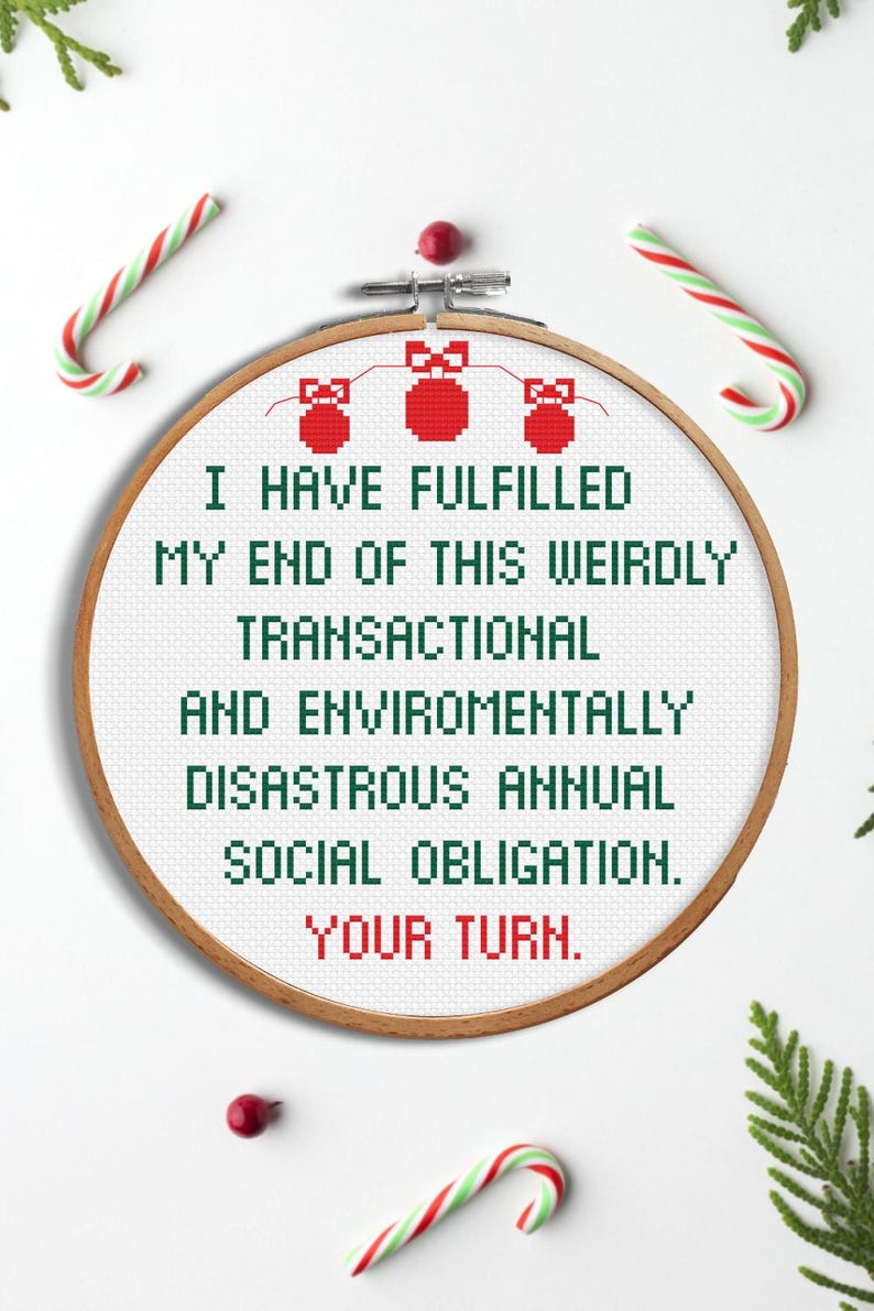 Op de afbeelding: Een borduurring met de tekst "I HAVE FULFILLED MY END OF THIS WEIRDLY TRANSACTIONAL AND ENVIROMENTALLY DISASTROUS ANNUAL SOCIAL OBLIGATION. YOUR TURN." Rode en groene zuurstokken en takjes omringen de ring.