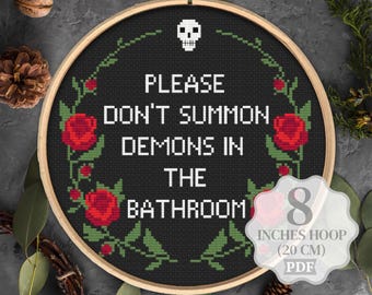 May include: Cross stitch pattern for an 8 inch hoop featuring a black and white skull with the text "Please don't summon demons in the bathroom". The pattern is surrounded by red roses and green leaves.