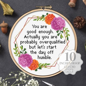 May include: Cross stitch pattern featuring a floral design with pink and orange flowers. The pattern includes the text "You are good enough. Actually you are probably overqualified but let's start the day off humble." and a note that the pattern is for a 10 inch hoop (25 cm).
