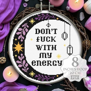 Może przedstawiać: Tamborek do haftu krzyżykowego z napisem "DON'T FUCK WITH MY ENERGY". Projekt zawiera półksiężyc, gwiazdy i elementy kwiatowe w kolorze czarnym i fioletowym. Tamborek ma średnicę 20 cm.