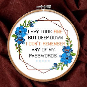 May include: A round wooden embroidery hoop containing white fabric with a cross-stitch design. The text reads I MAY LOOK FINE BUT DEEP DOWN I DON'T REMEMBER ANY OF MY PASSWORDS. It features blue flowers, green leaves, and a geometric copper frame.