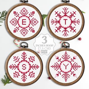 Peut inclure: Quatre cerceaux de broderie de 7,5 cm avec des motifs de flocons de neige rouges et une lettre au centre. Les lettres sont E, T, S et Y. Les cerceaux sont sur un fond blanc avec des cannes en sucre et de la verdure.