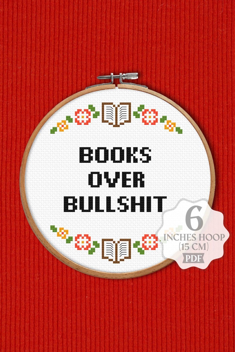 K&ouml;nnte beinhalten: Ein wei&szlig;er Stickrahmen mit einem Kreuzstich-Design, das "BOOKS OVER BULLSHIT" lautet. Das Design ist von einem Rand aus kleinen Blumen und B&uuml;chern umgeben. Der Rahmen hat einen Durchmesser von 15 cm.